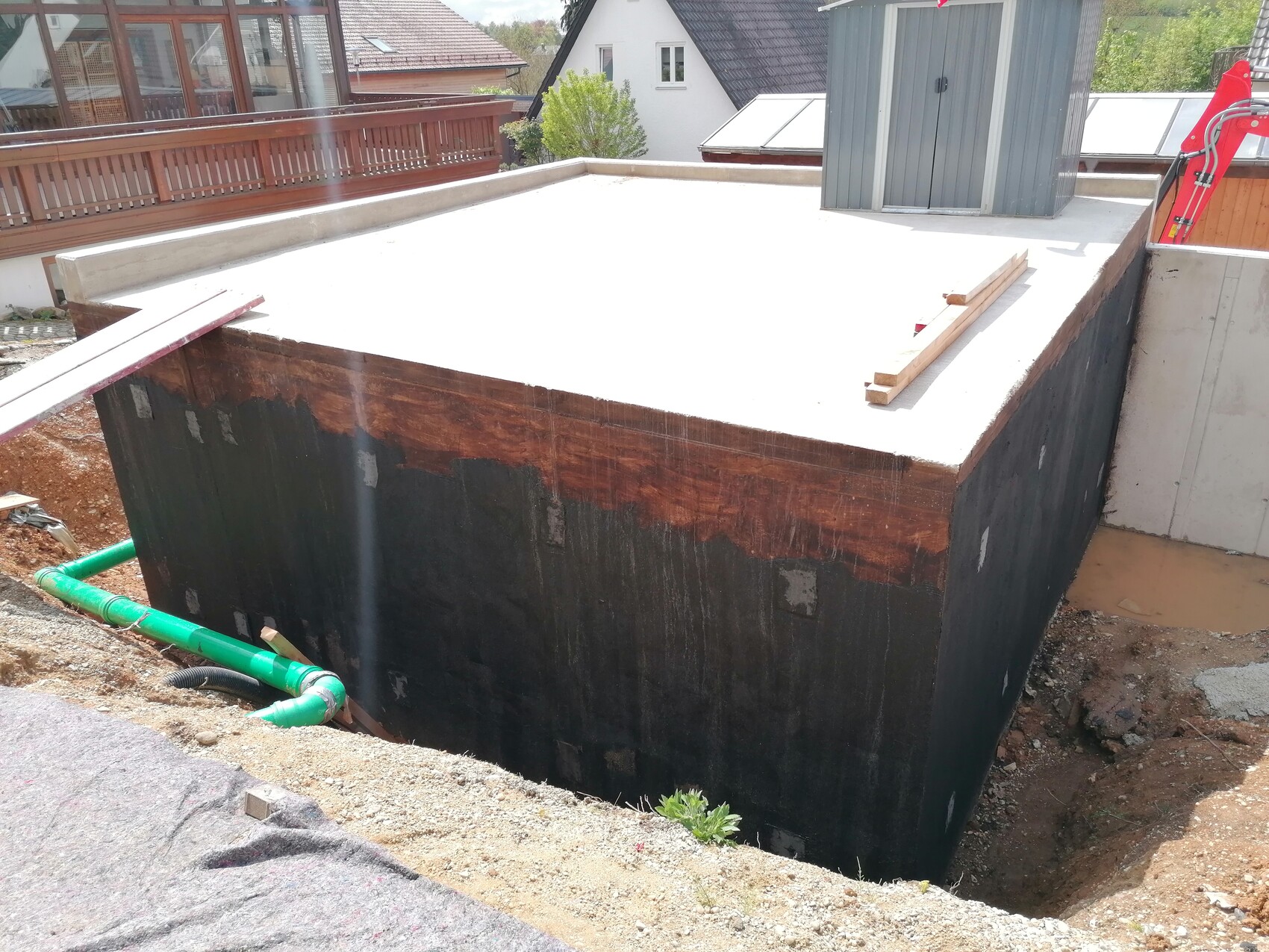 Kellerfundament auf Baustelle mit schwarzer Abdichtung, Holzformen und grünen Rohren