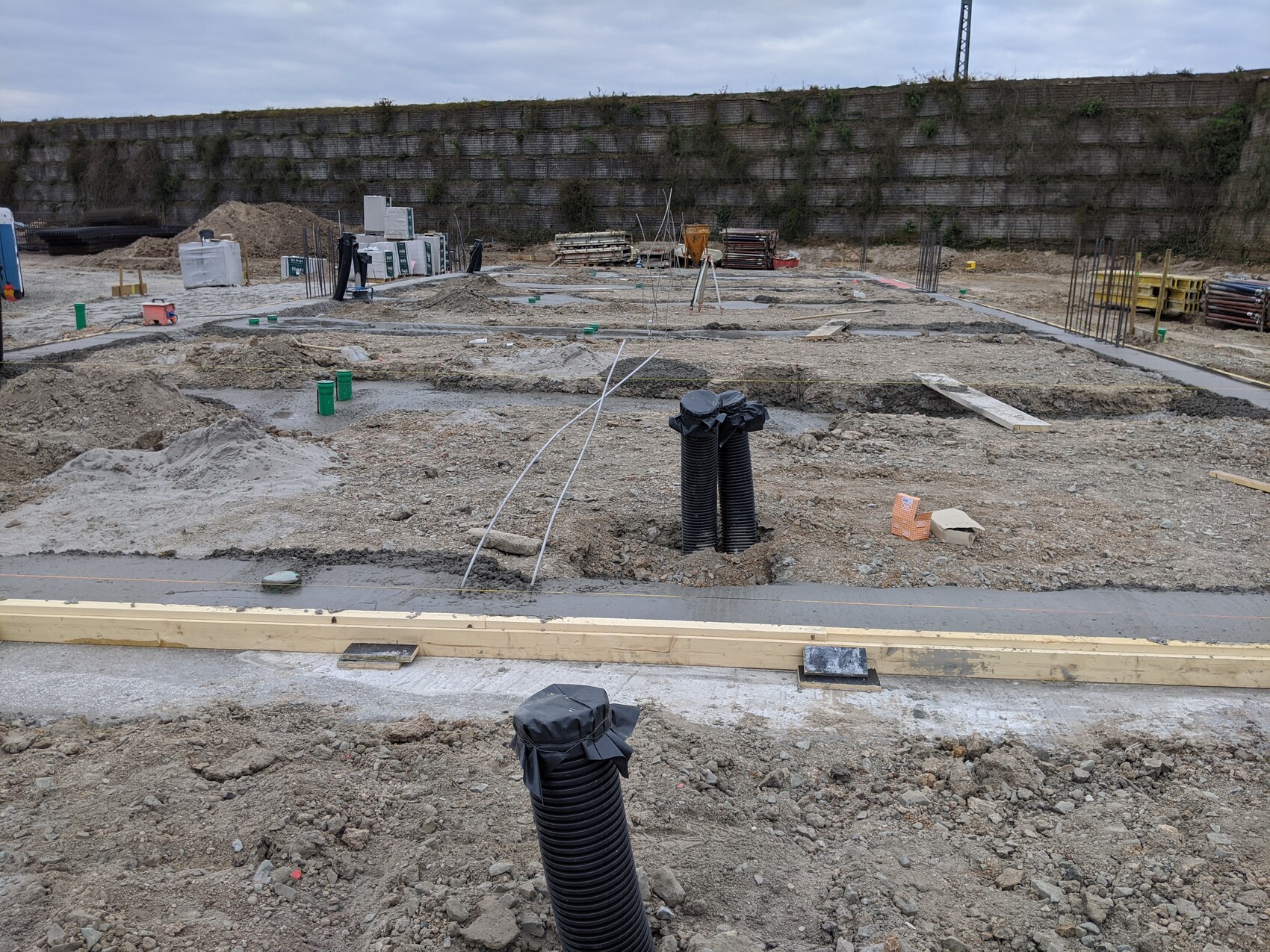 Baustelle mit Gräben, Fundamentarbeiten; schwarze Rohre ragen aus dem Boden.
