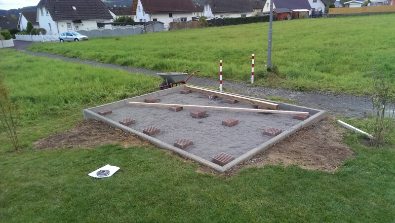 Kleines Baugrundstück mit Fundamentplatte, Bauarbeiten und Wohnhäusern im Hintergrund