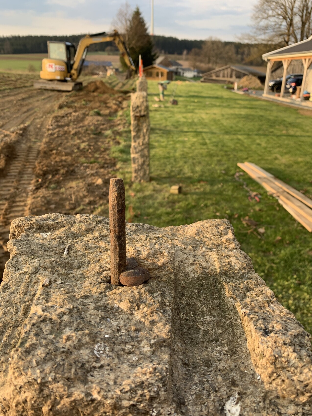 Rostiger Stahlstift in einem Betonblock; Baustelle mit Bagger im Hintergrund.