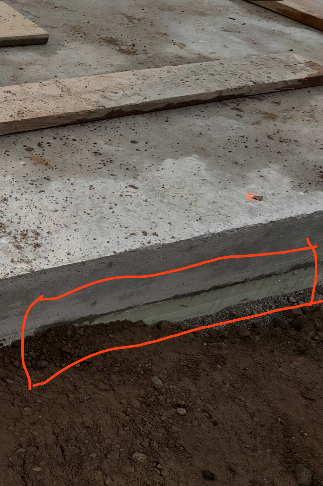 Baustellenaufnahme eines Fundaments mit Betonboden, Erdreich und oranger Markierung.