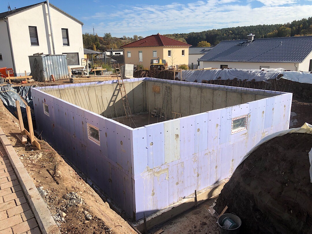 Rohbau-Fundament mit blauer Dämmung in Baugrube und Leitern auf der Baustelle