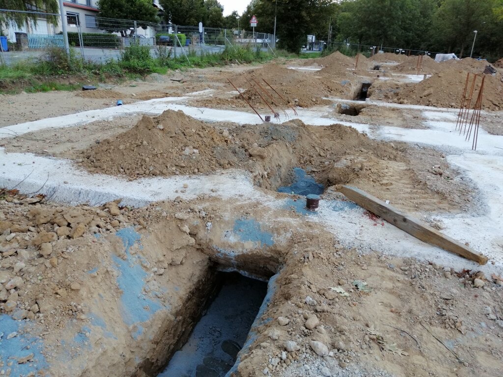 Baustelle mit offenen Gräben, Erdarbeiten, Bewehrungsstahl und Holzplanke.