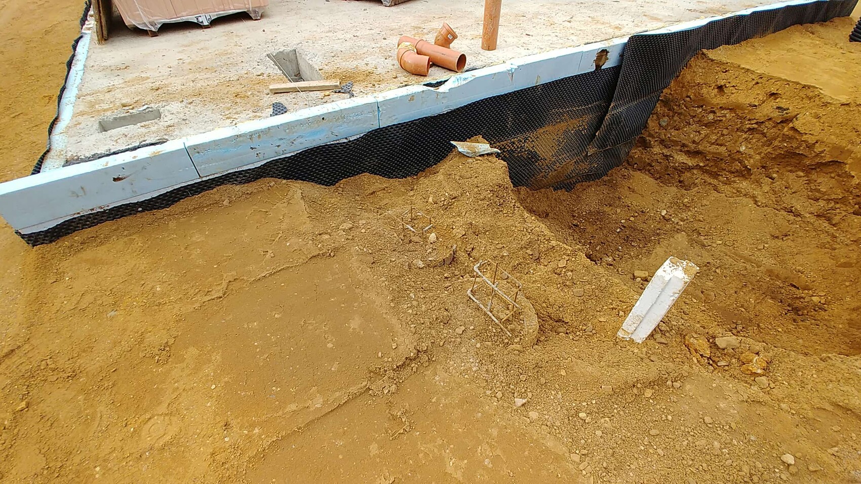 Fundamentgraben auf Baustelle mit Drainagebahn und Erdarbeiten