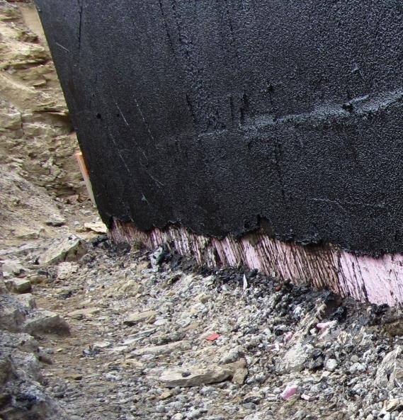 Fundamentunterkante mit schwarzer Dichtungsbahn und sichtbarer Dämmung an einer Baustelle