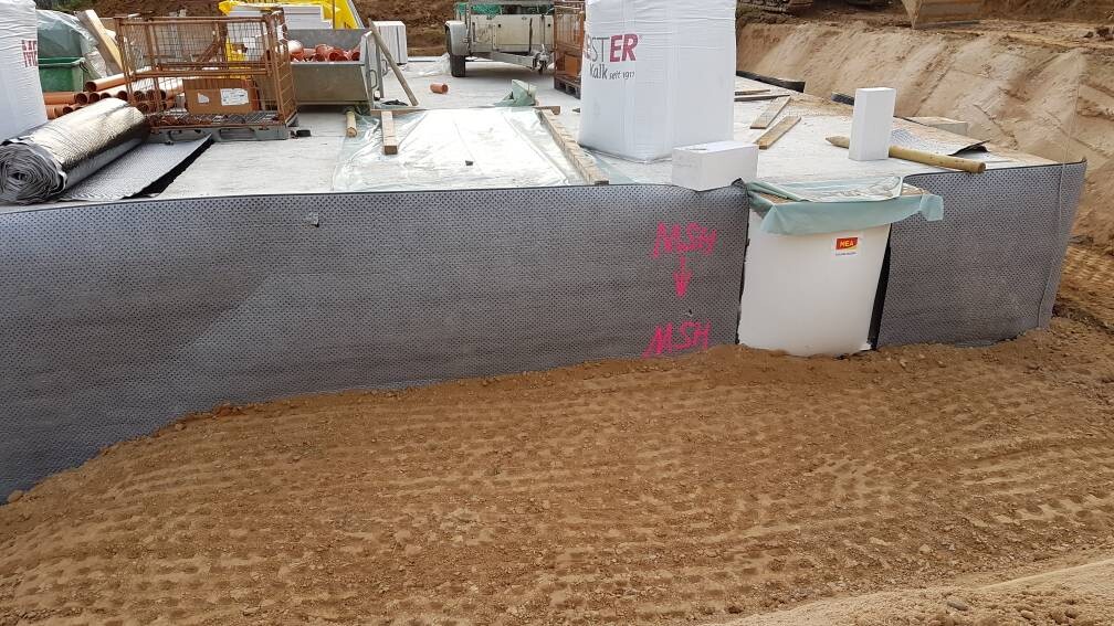 Baustelle: Fundamentplatte, schwarze Dichtbahn, Materialkörbe, Erdaushub davor.