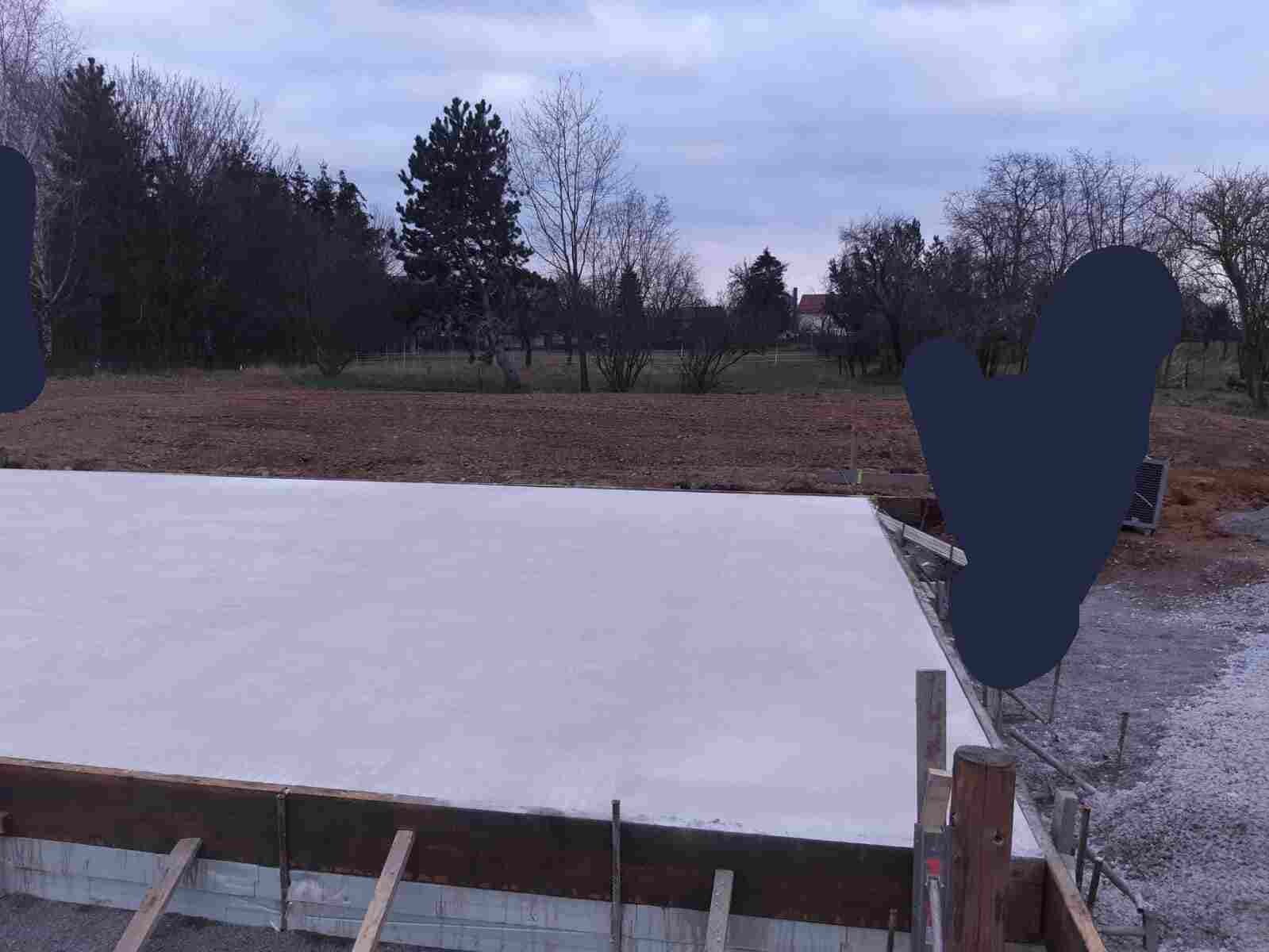 Betonplatte auf Holzformen einer Baustelle, Hintergrund mit Bäumen und wolkigem Himmel.
