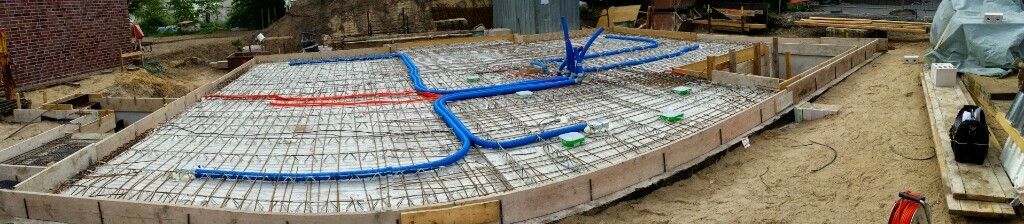 Fundament mit Bewehrungsgitter und blauen sowie roten Rohren auf der Baugrube.