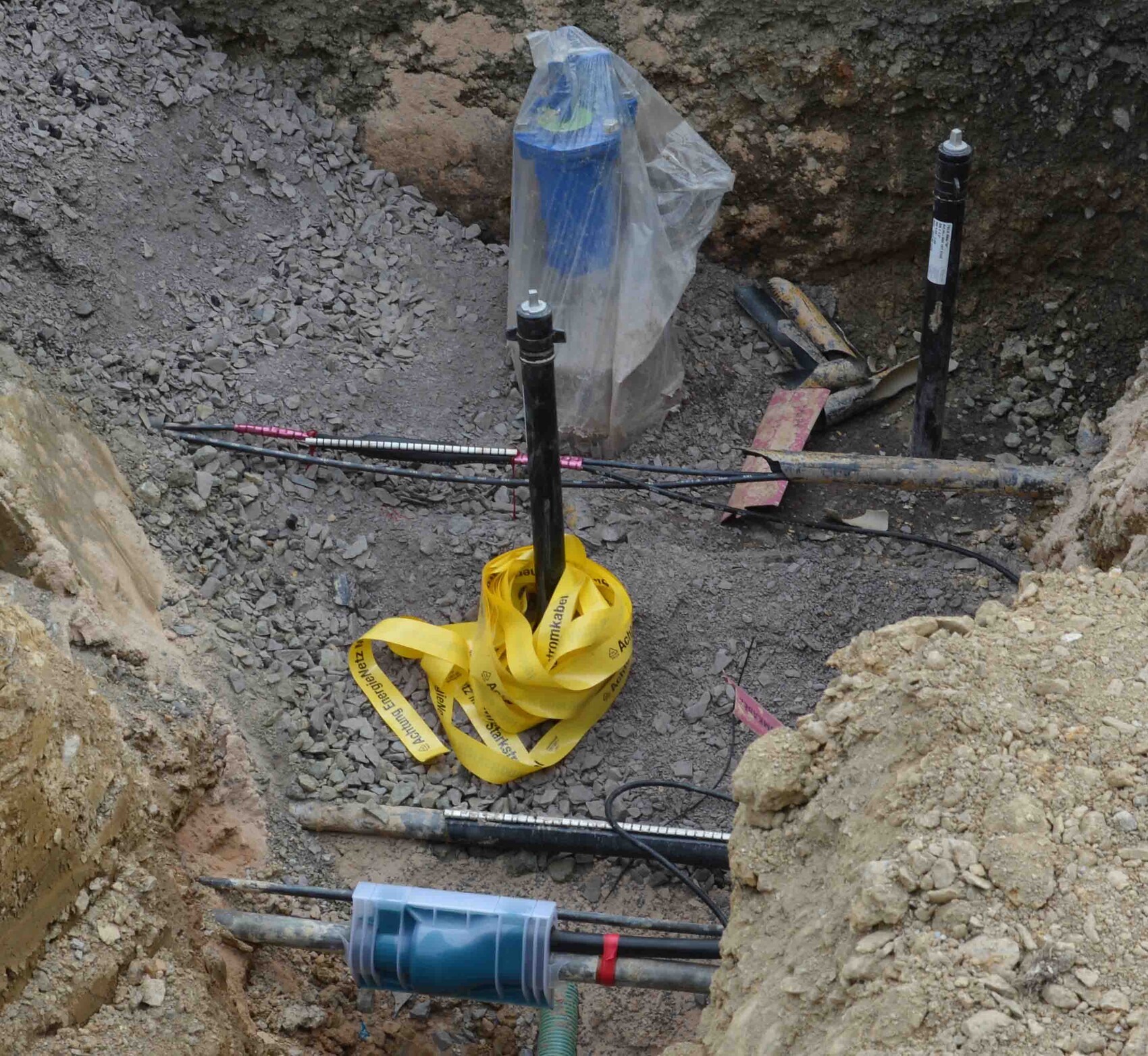 Baugrube mit Rohbaufundament, Rohren, gelbem Absperrband und Baumaschinen.