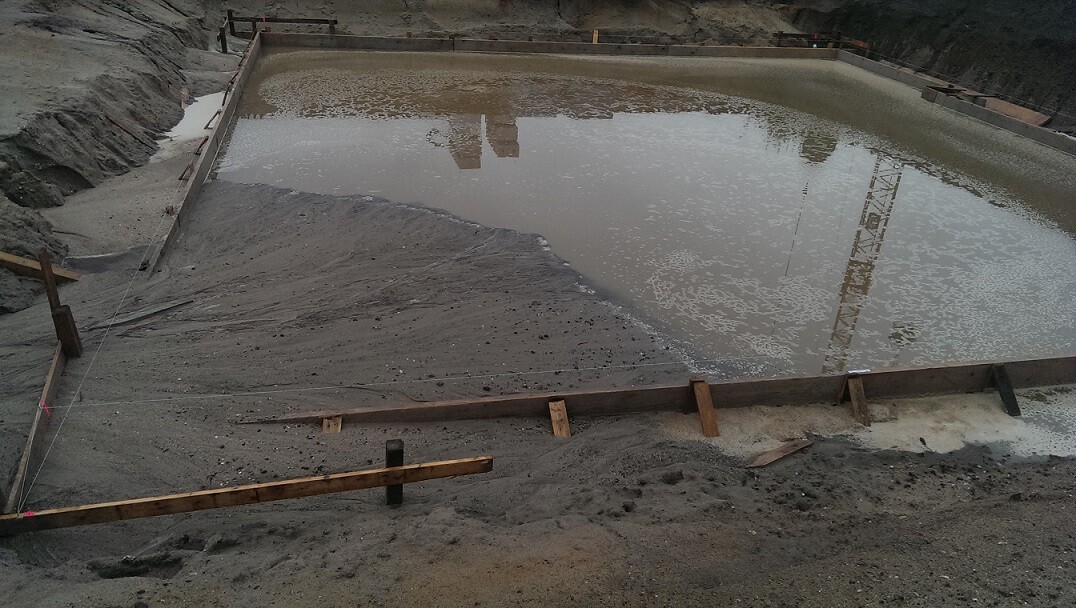 Fundamentgrube mit Wasser und Holzformrahmen auf Baustelle