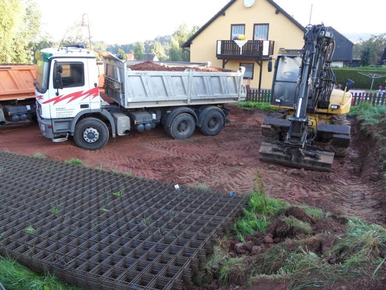Baustelle: Kipp-LKW entlädt Erdreich, Bagger gräbt, Bewehrungsgitter liegt auf dem Boden