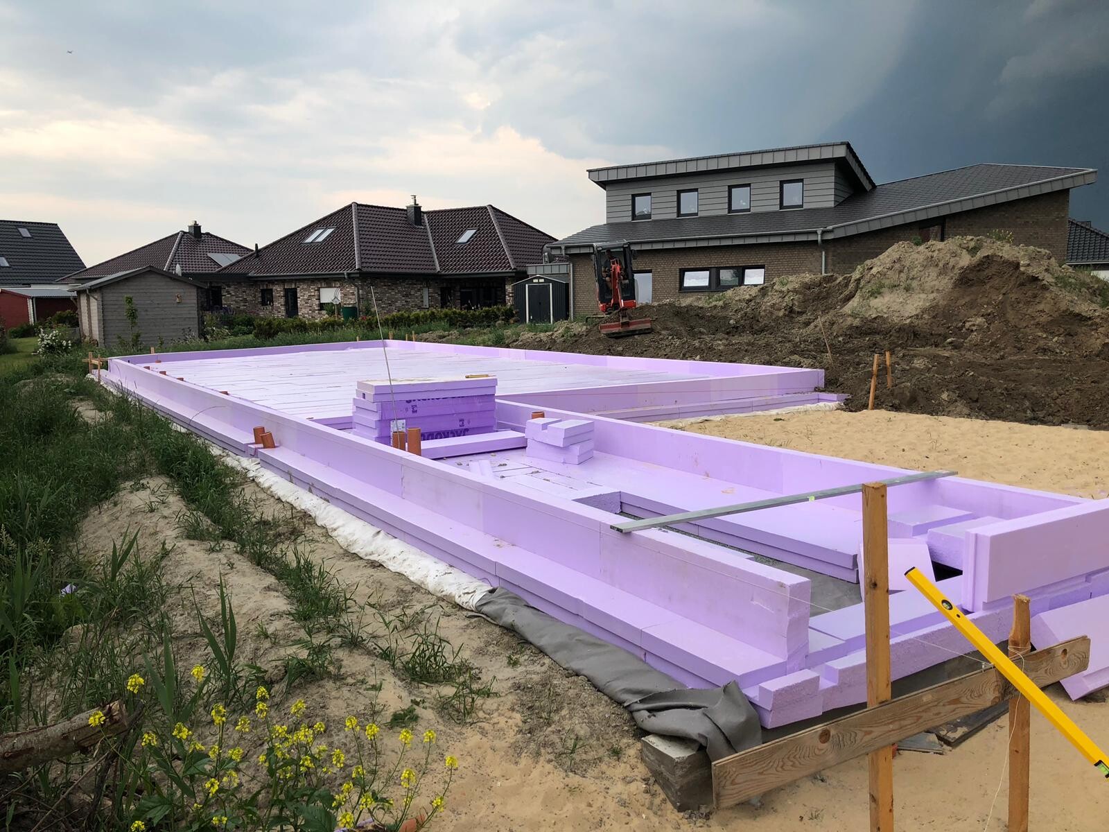 Fundamentbau mit lavendelfarbenen Dämmplatten aus Polystyrol; Bagger auf Sandhügel.