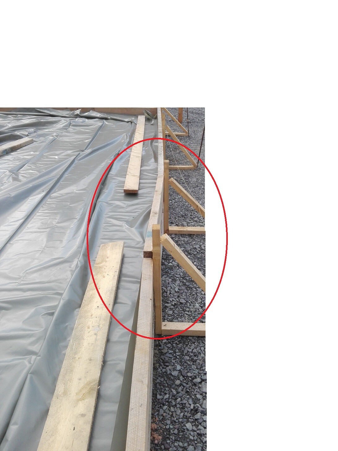 Baustelle mit Holzrahmen für Fundament, Plastikfolie bedeckt, Kiesboden sichtbar