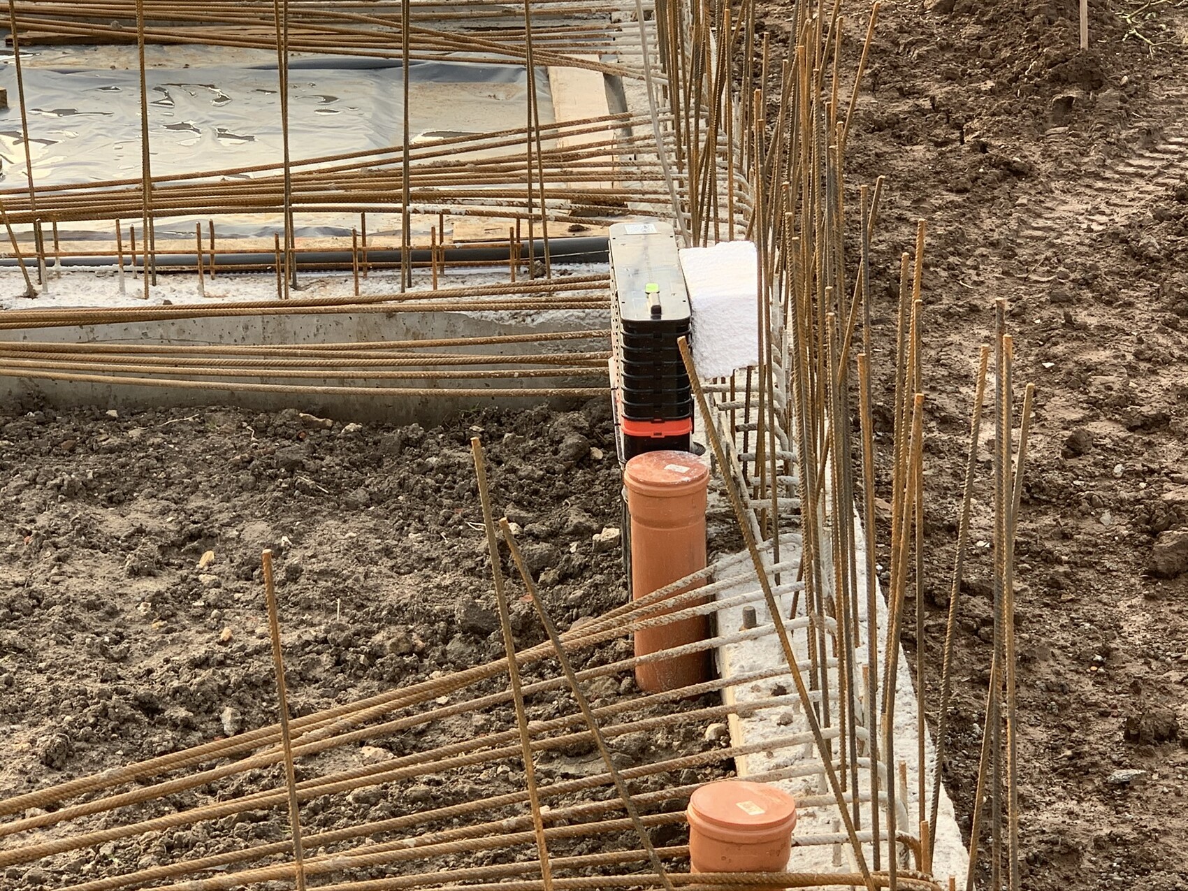 Baustelle mit Stahlbewehrung im Graben, Betonfundament und Erdreich.