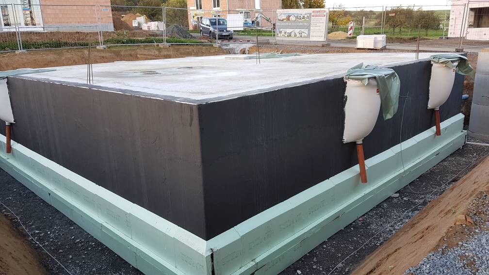 Großes schwarzes, rechteckiges Bauelement auf grüner Styropor-Isolierung, Baustelle; seitliche Rohre.