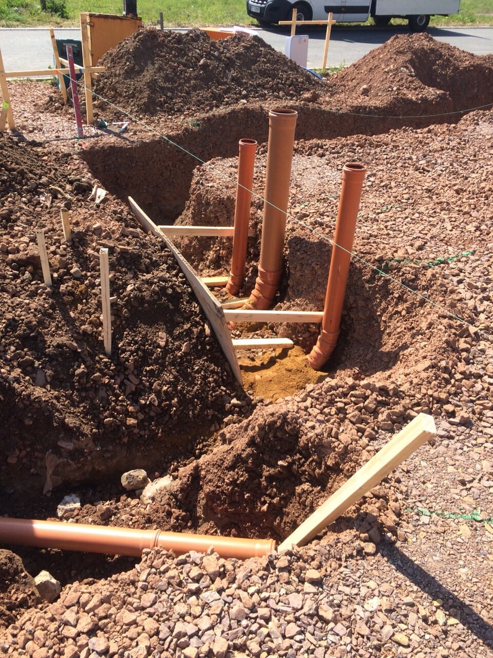 Baustelle: Graben mit orangefarbenen Abflussrohren, Holzgestell und Erde.