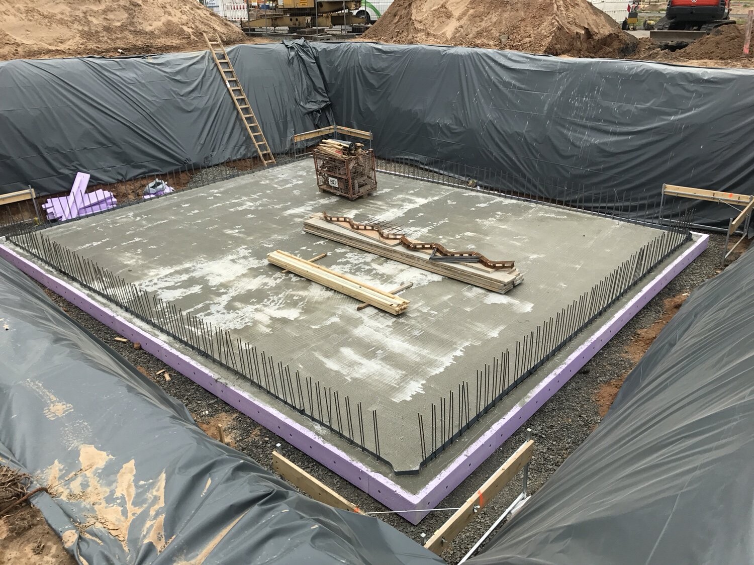 Fundamentplatte aus Beton mit umlaufender Bewehrung am Rand, von Baufolie umgeben auf der Baustelle.