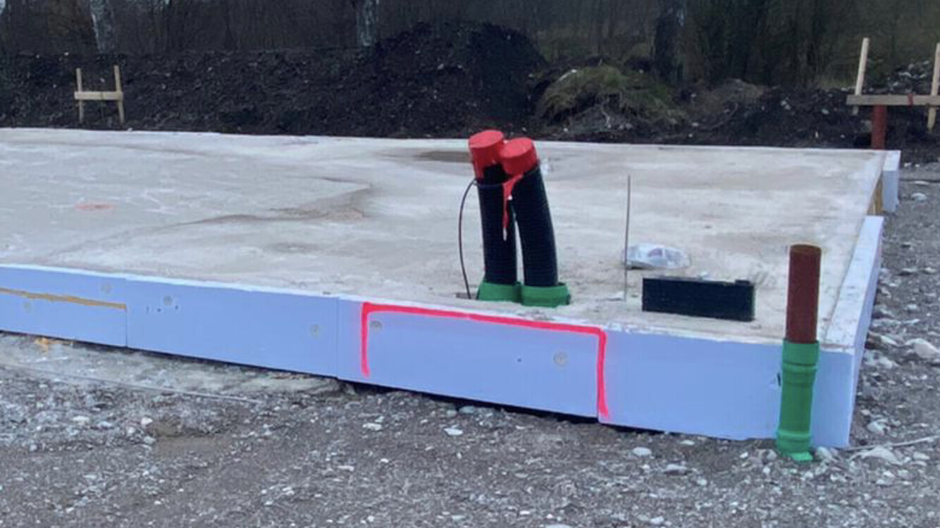 Fundamentplatte auf einer Baustelle mit blauer Dämmung, schwarzen Rohren mit roten Enden