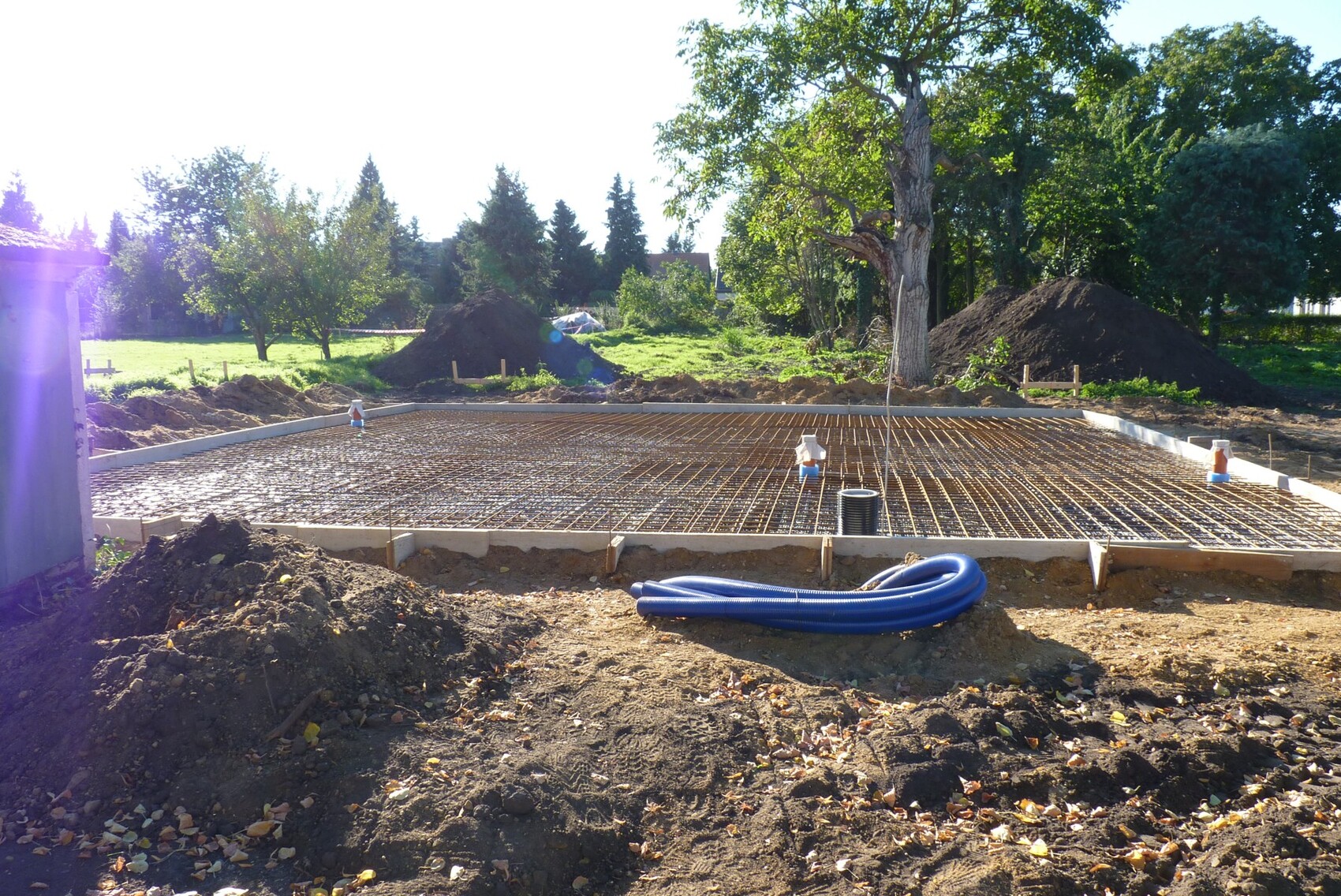 Fundament mit Bewehrungsstahlgitter, blaue Schläuche liegen im Vordergrund, Bäume im Hintergrund