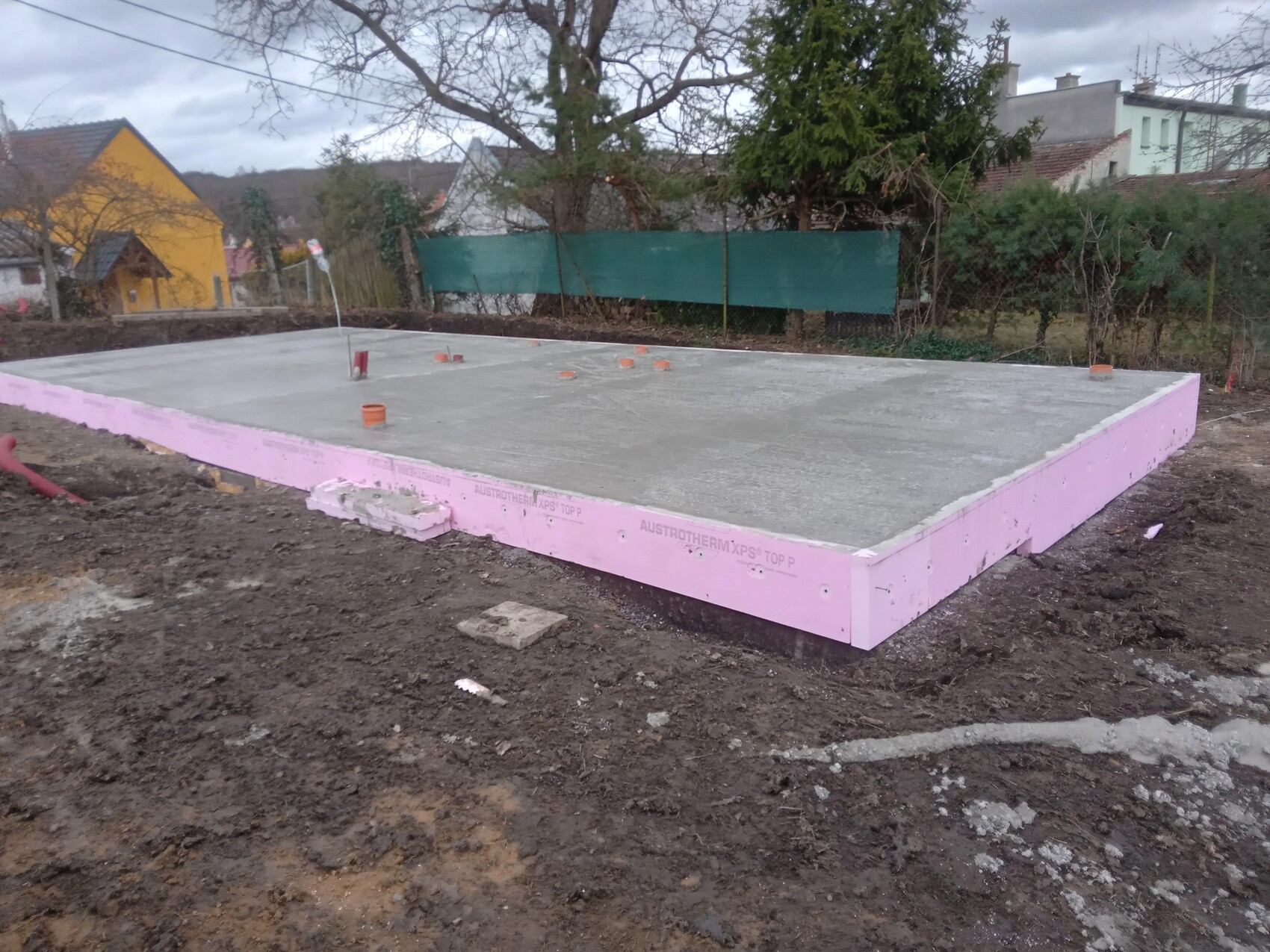 Grundplatte aus frischem Beton mit pinkem Styrodurrand und orange Rohre.