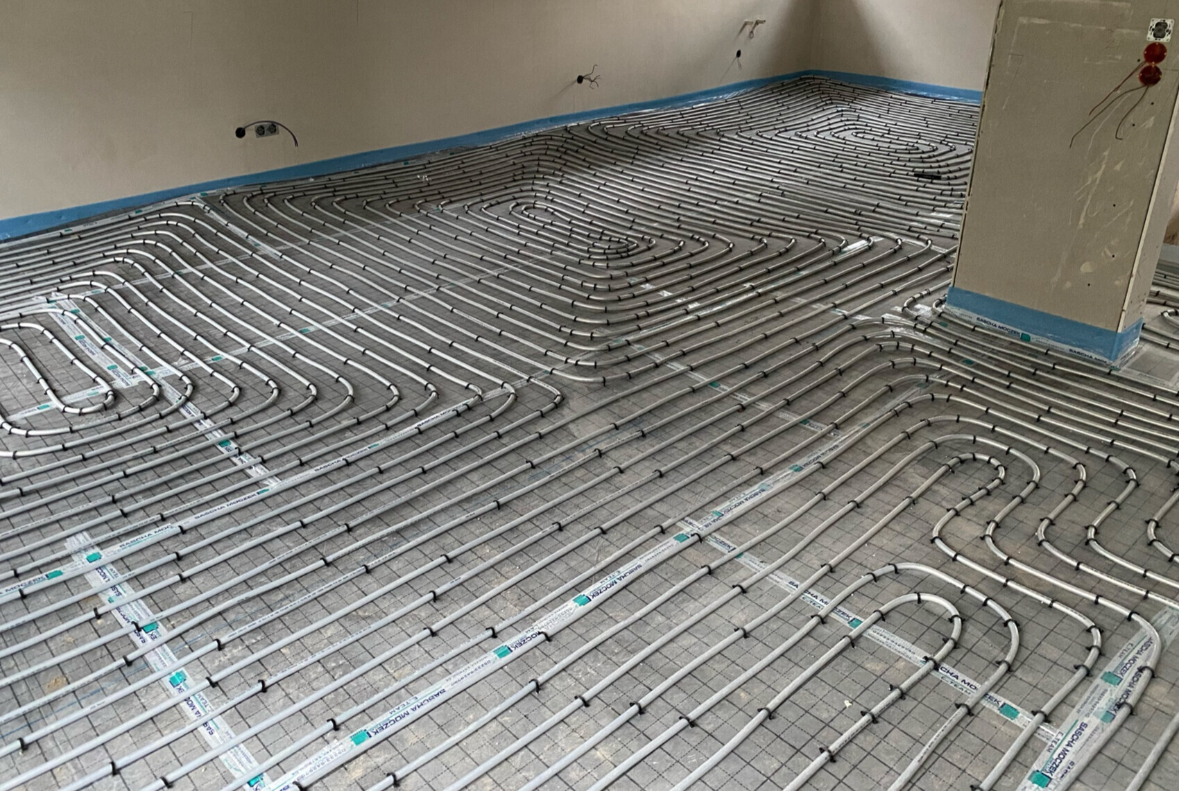 Fußbodenheizung: Heizrohre in Schleifen auf einer Metallmatte im Bauzimmer.