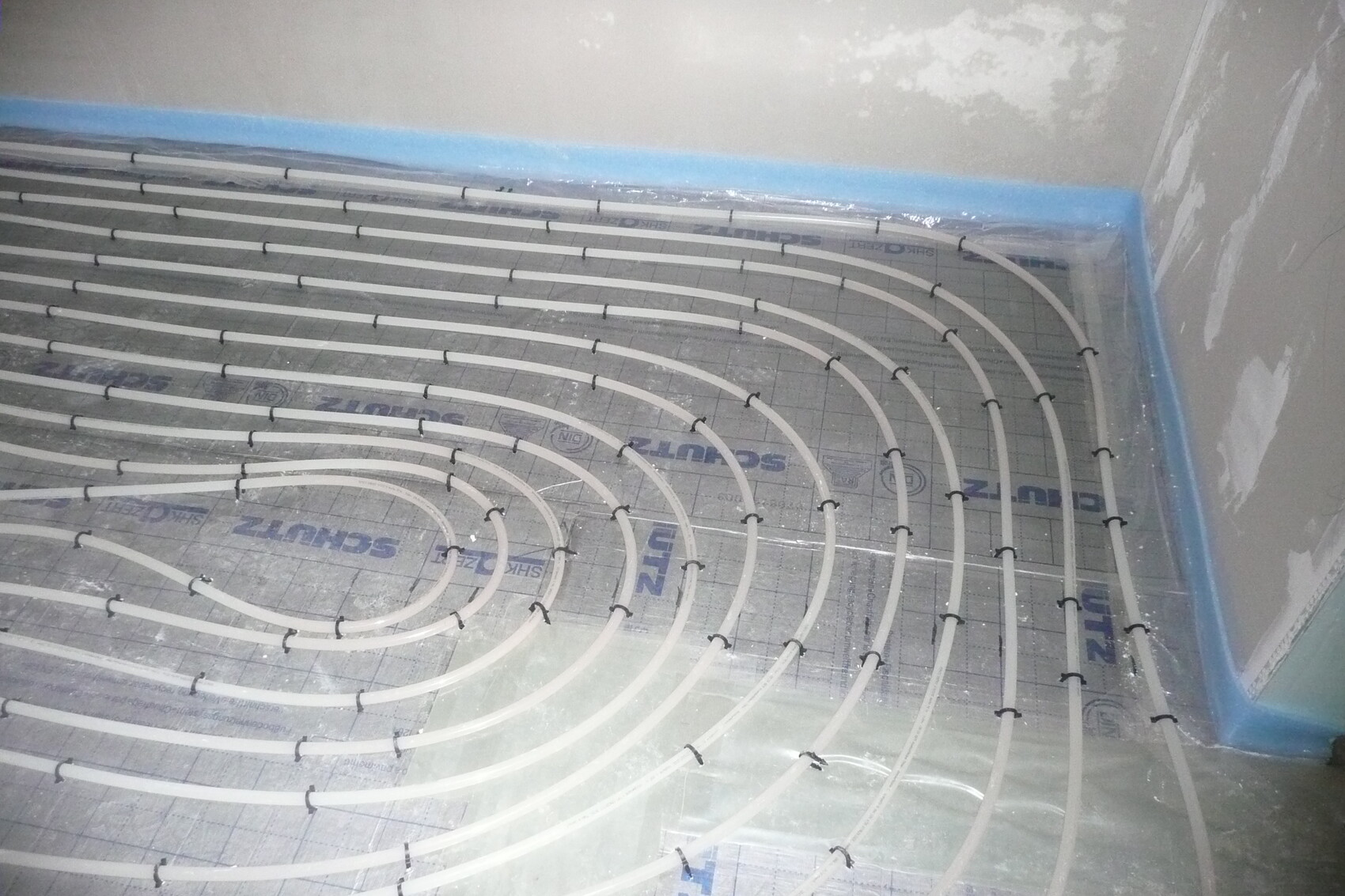 Fußbodenheizung: spiralförmige Heizrohre auf Dämmplatten verlegt, Baufortschritt sichtbar.