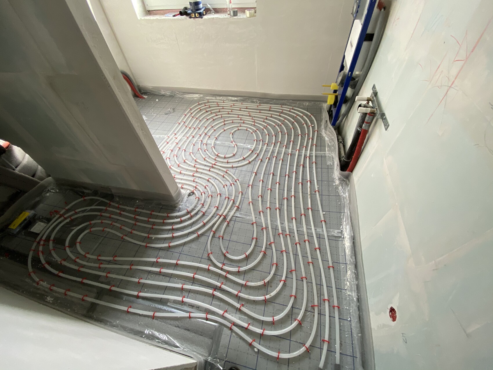 Fußbodenheizung: Verlegte weiße Rohrschlangen in Spiralen auf einer Baustellenbodenplatte.