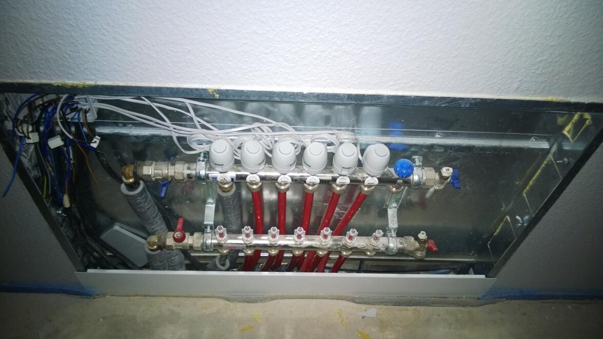 Heizungs-Verteiler mit roten Rohren, Ventilen und Kabeln in einem Metallgehäuse.