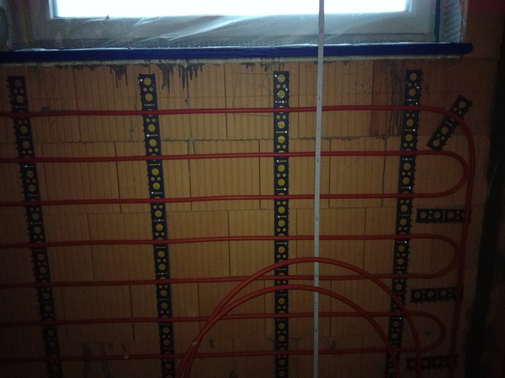 Rote Heizungsrohre verlaufen an einer Wand im Bau, Installationsmaterial sichtbar.
