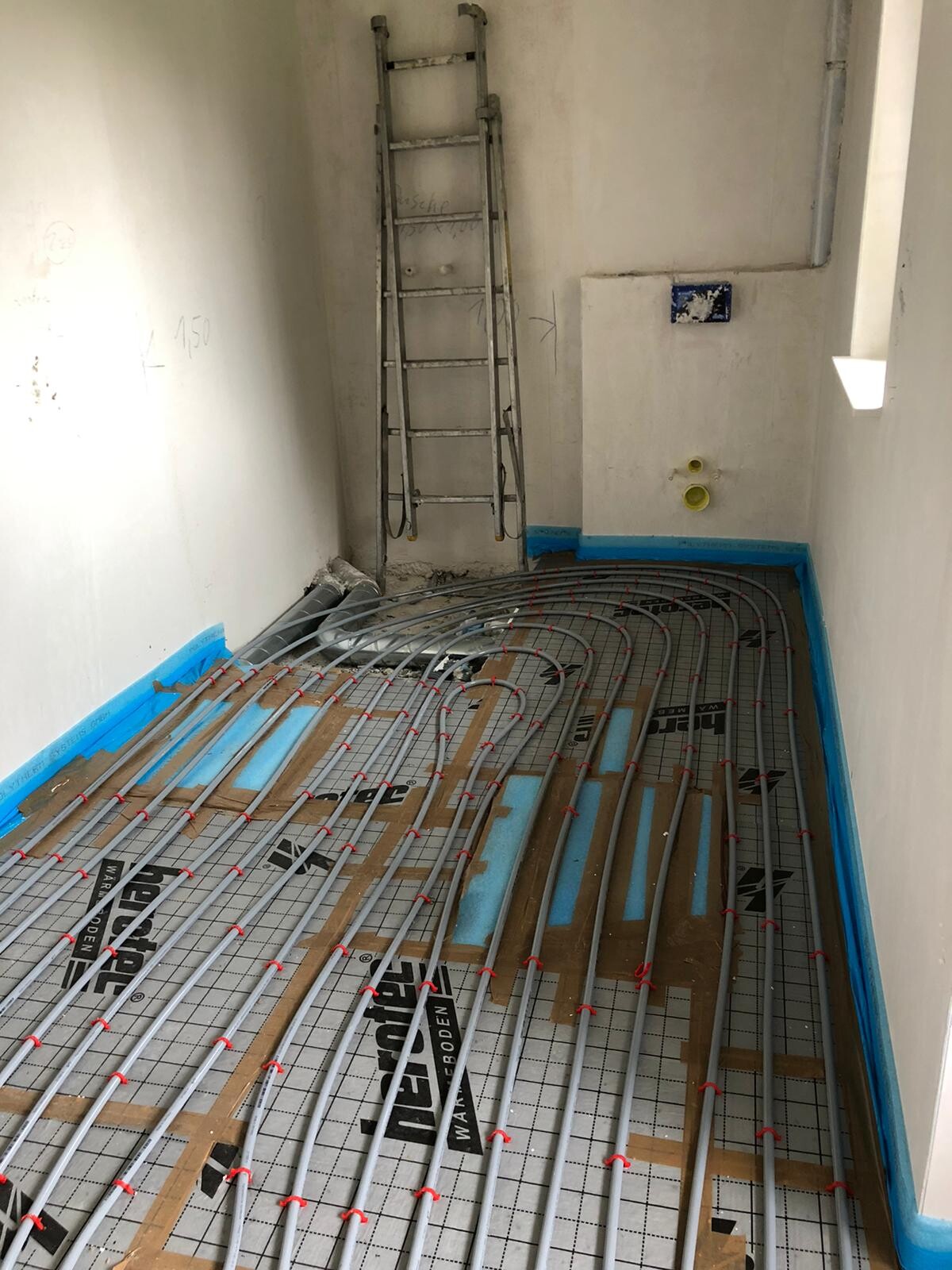 Bauraum mit Unterbodenheizung: Heizrohre auf Dämmunterlage, Leiter an der Wand.