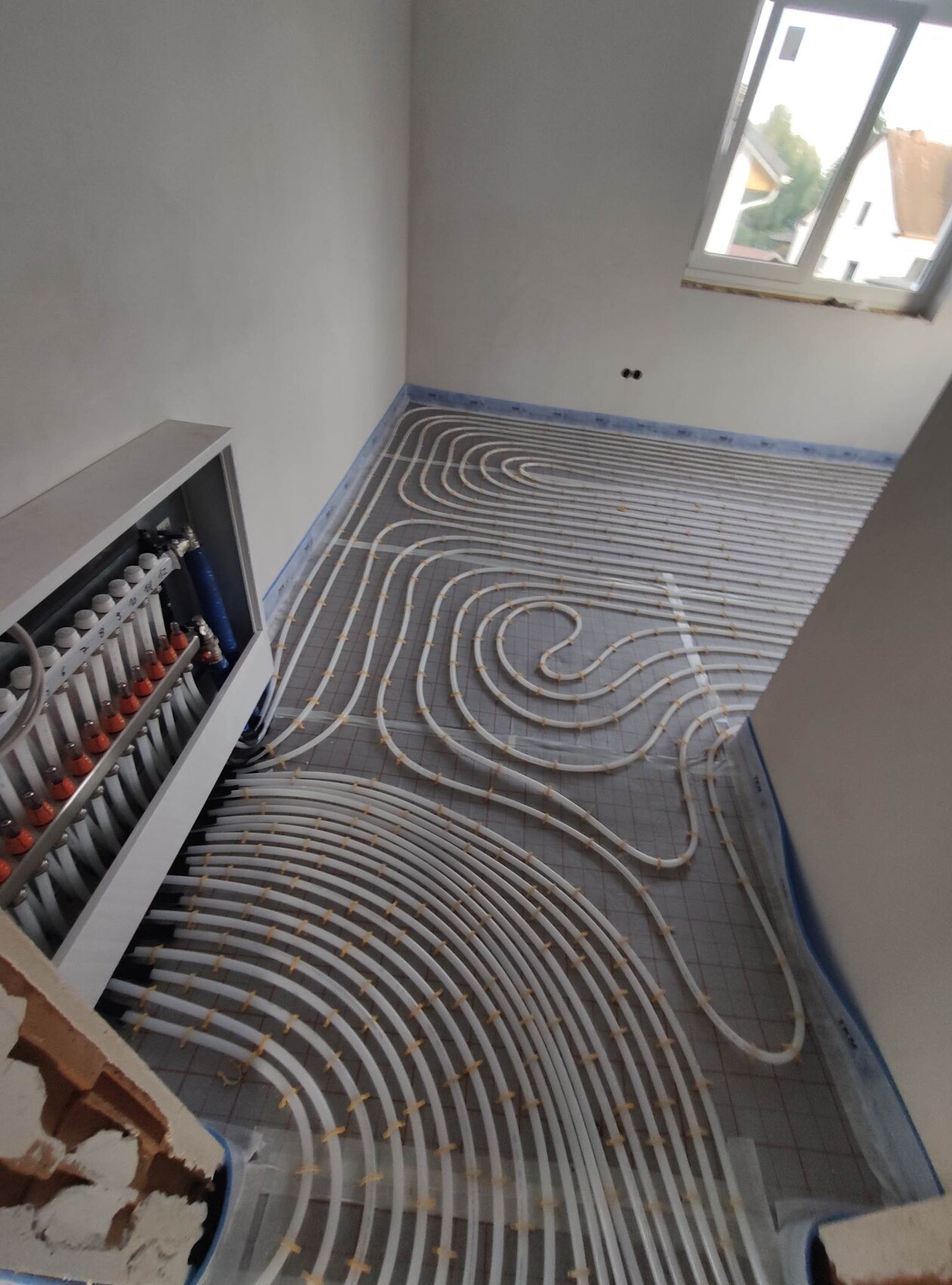 Unterflur-Heizungsschläuche werden spiralförmig im Neubau-Raum verlegt, linke Verteilstation sichtbar.