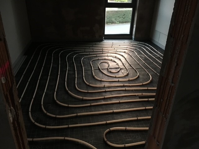 Spiralförmige Unterbodenheizungsrohre auf dem Boden eines Bauprojekts; Fenster im Hintergrund.