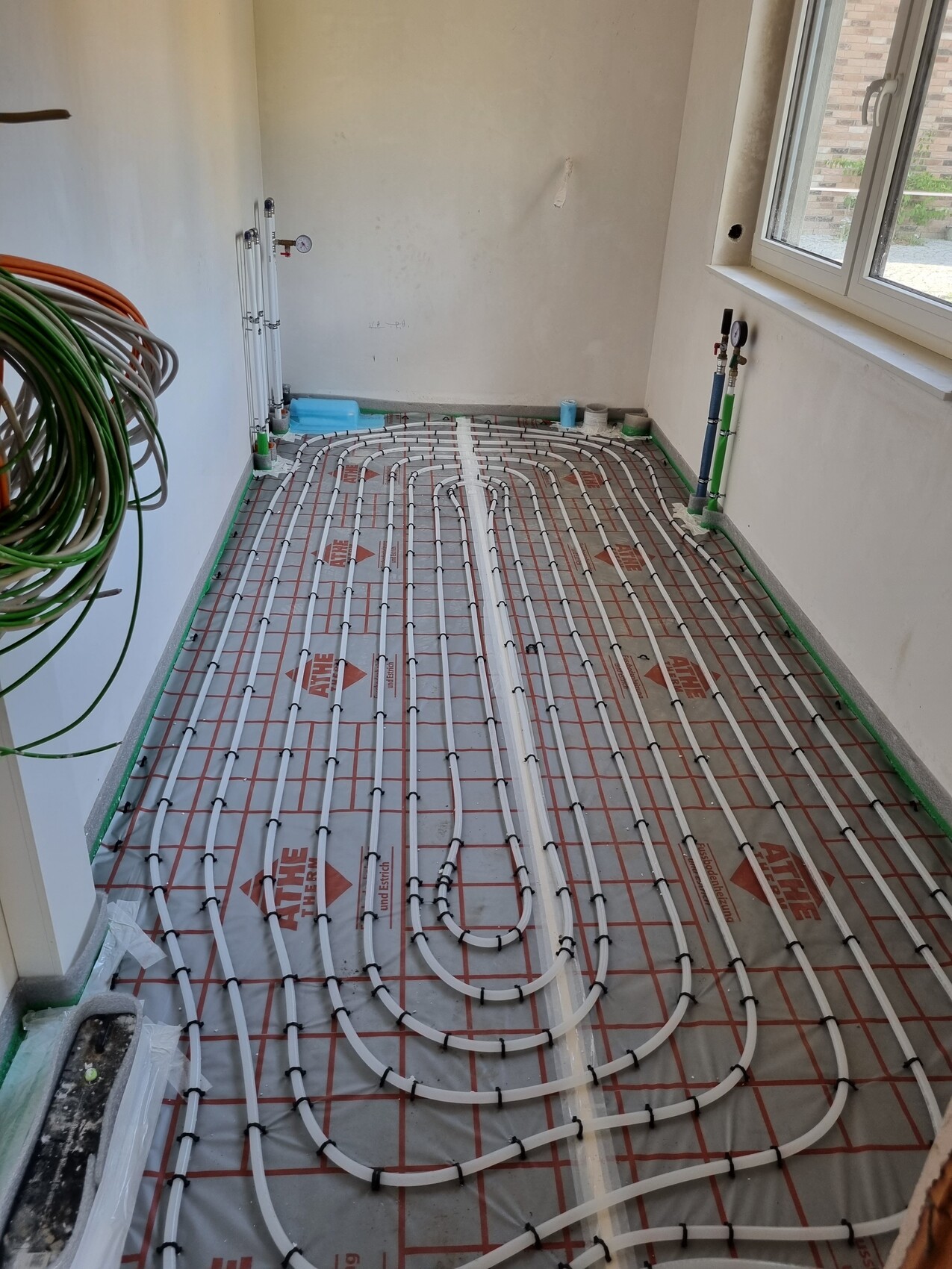 Unterflur-Heizsystem: Verlegte Heizrohre auf Dämmunterlage in einem Renovierungsraum, Fenster rechts.