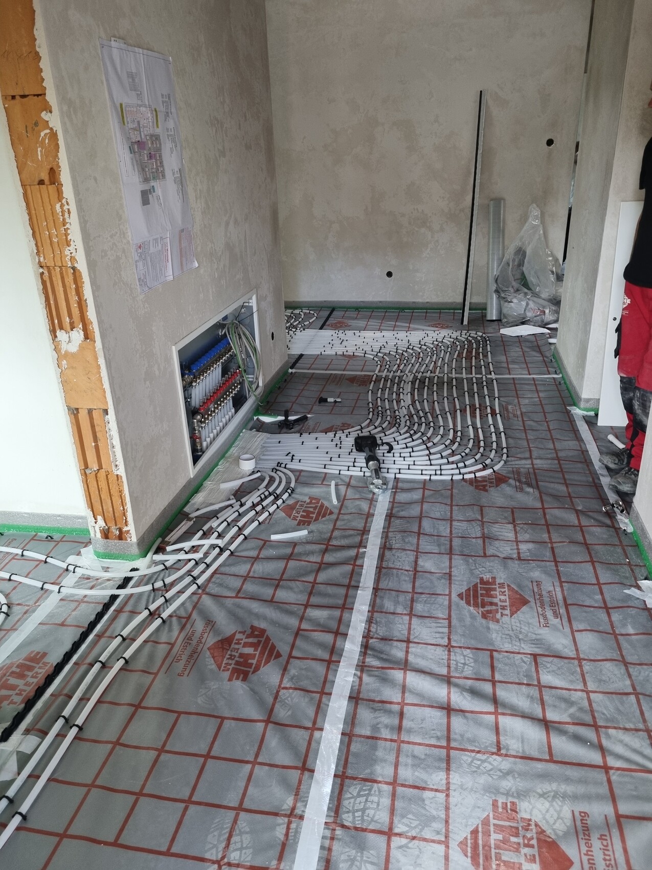 Unterflurheizung: Rohre verlegt auf Dämmunterlage, Wandverteiler sichtbar im Bauzimmer.