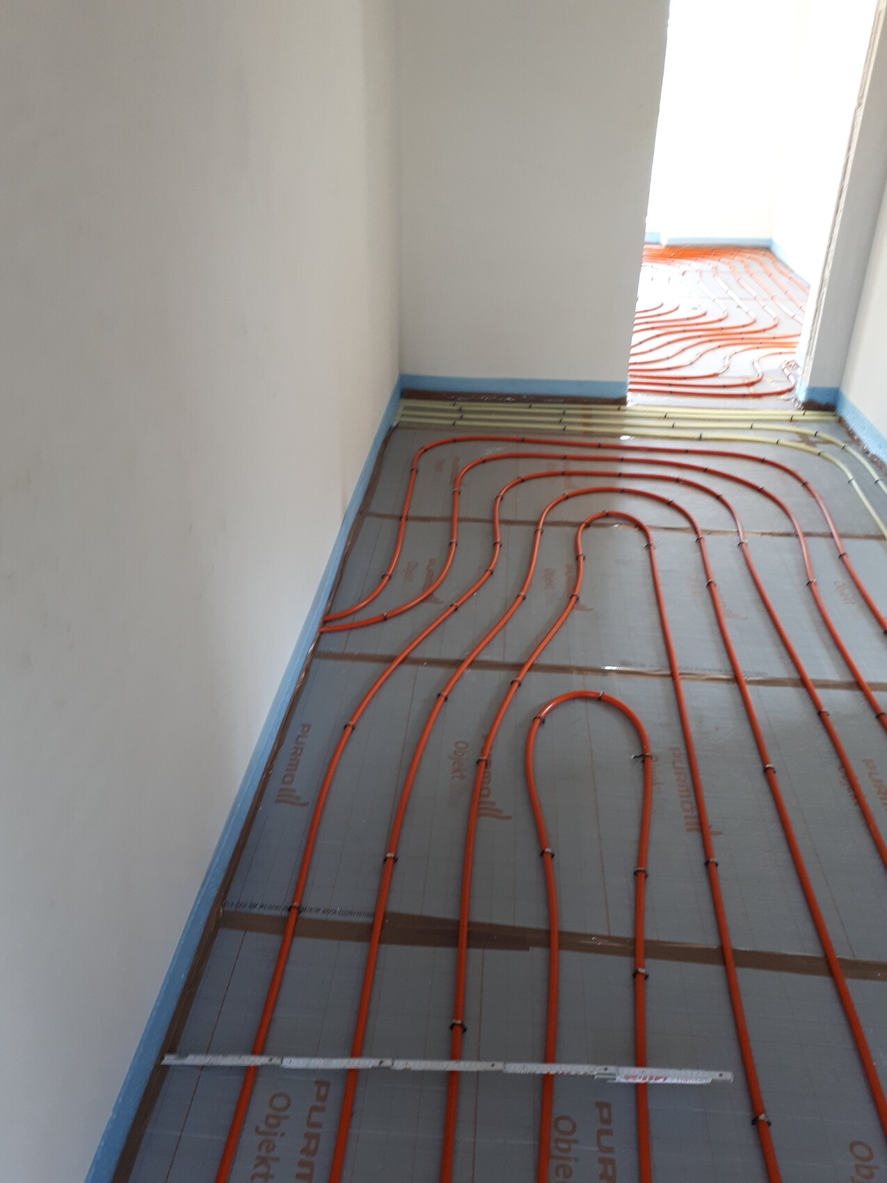 Orange Fußbodenheizungsschläuche verlegt auf Dämmplatten in einem Neubauzimmer.