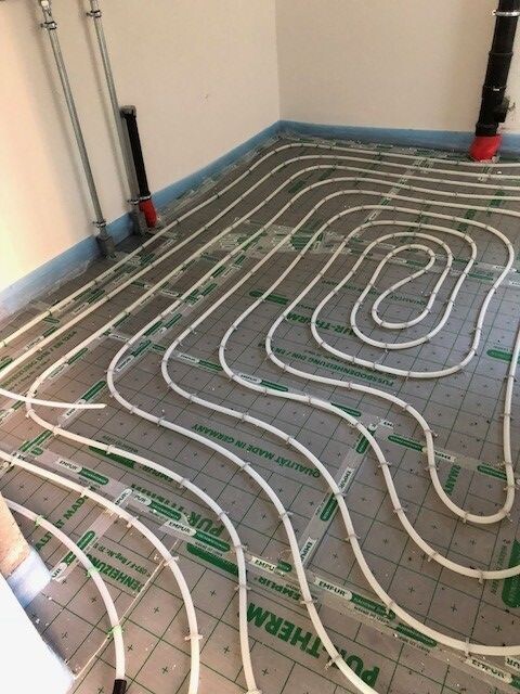 Fußbodenheizung: Weiße Heizrohre in Spiralen auf Dämmplatten verlegt, bereit für Estrich.