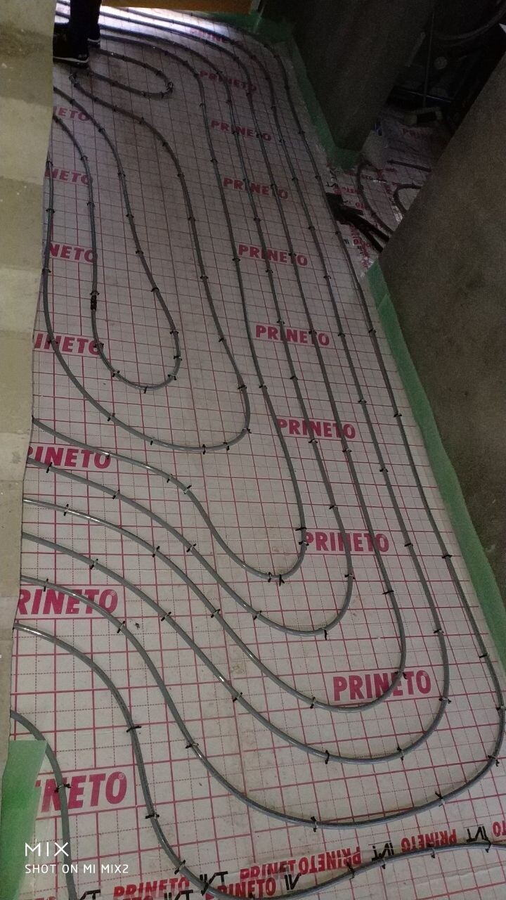 Unterflur-Heizrohre in Schlaufen auf Dämmplatten mit Rastergrid, Baustellenansicht.