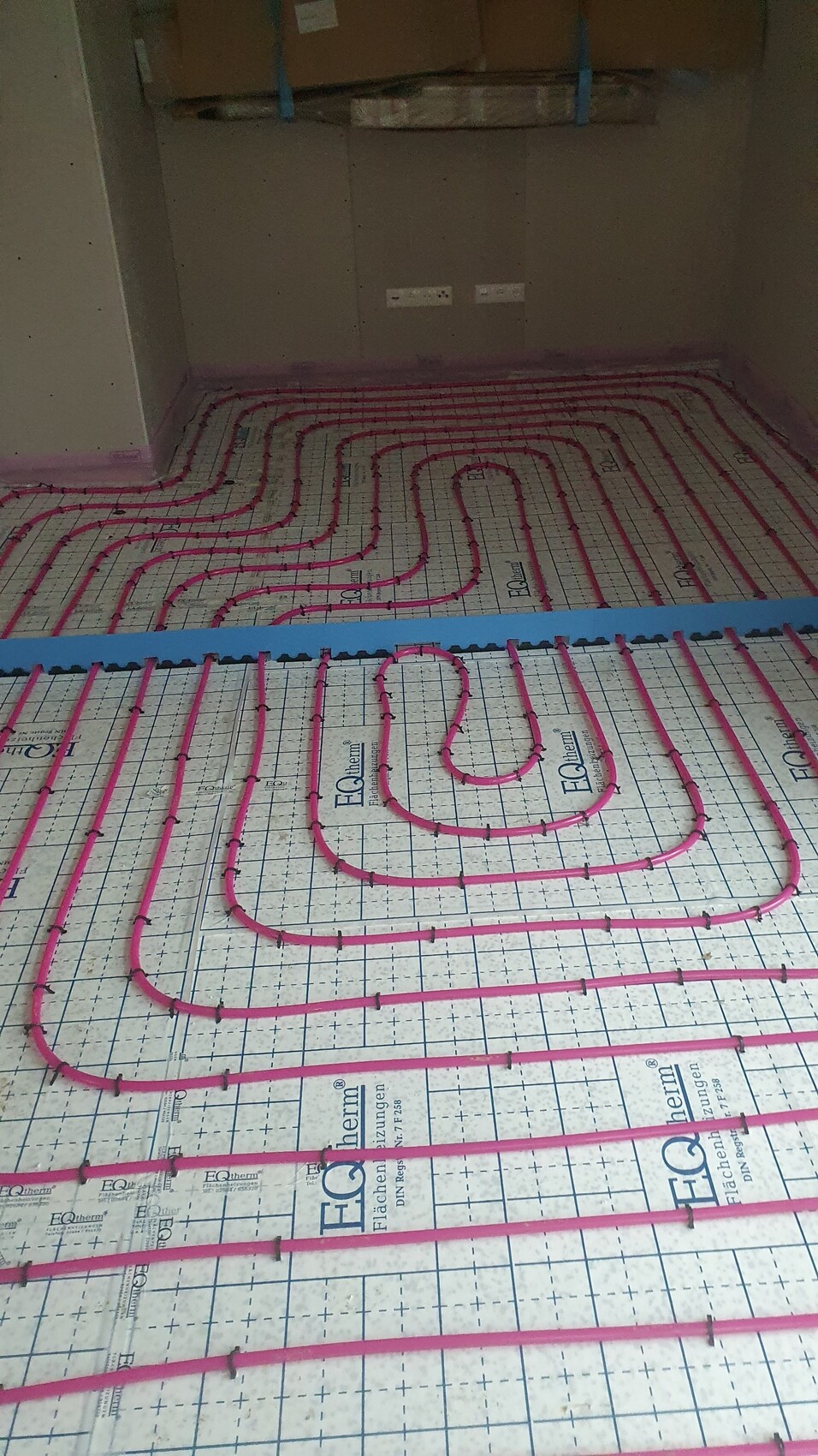 Unterbodenheizung: pinke Heizleitungen in Spiralen auf Dämmplatten im Rohbau.
