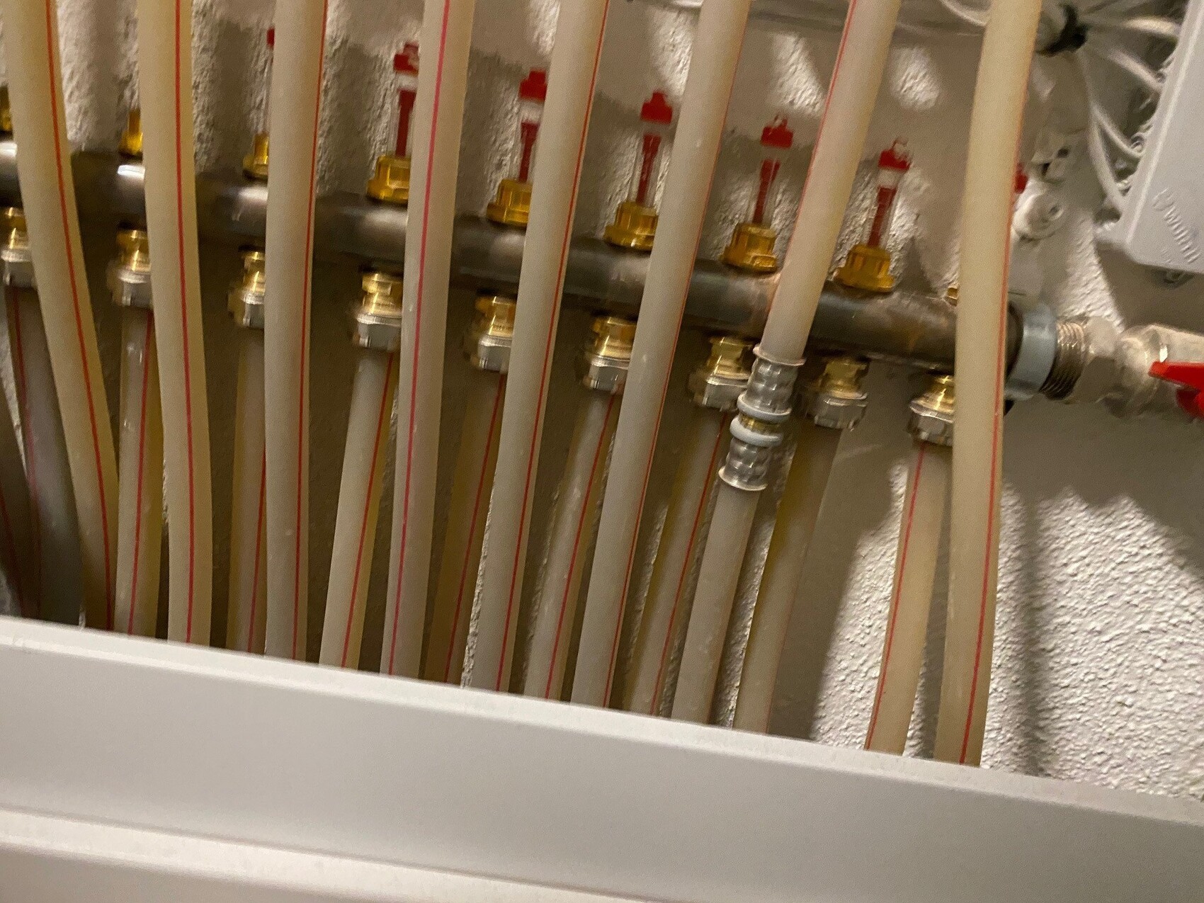 Mehrere beige PEX-Rohre mit roter Markierung, an Metall-Verteiler mit Messing-Fittings.