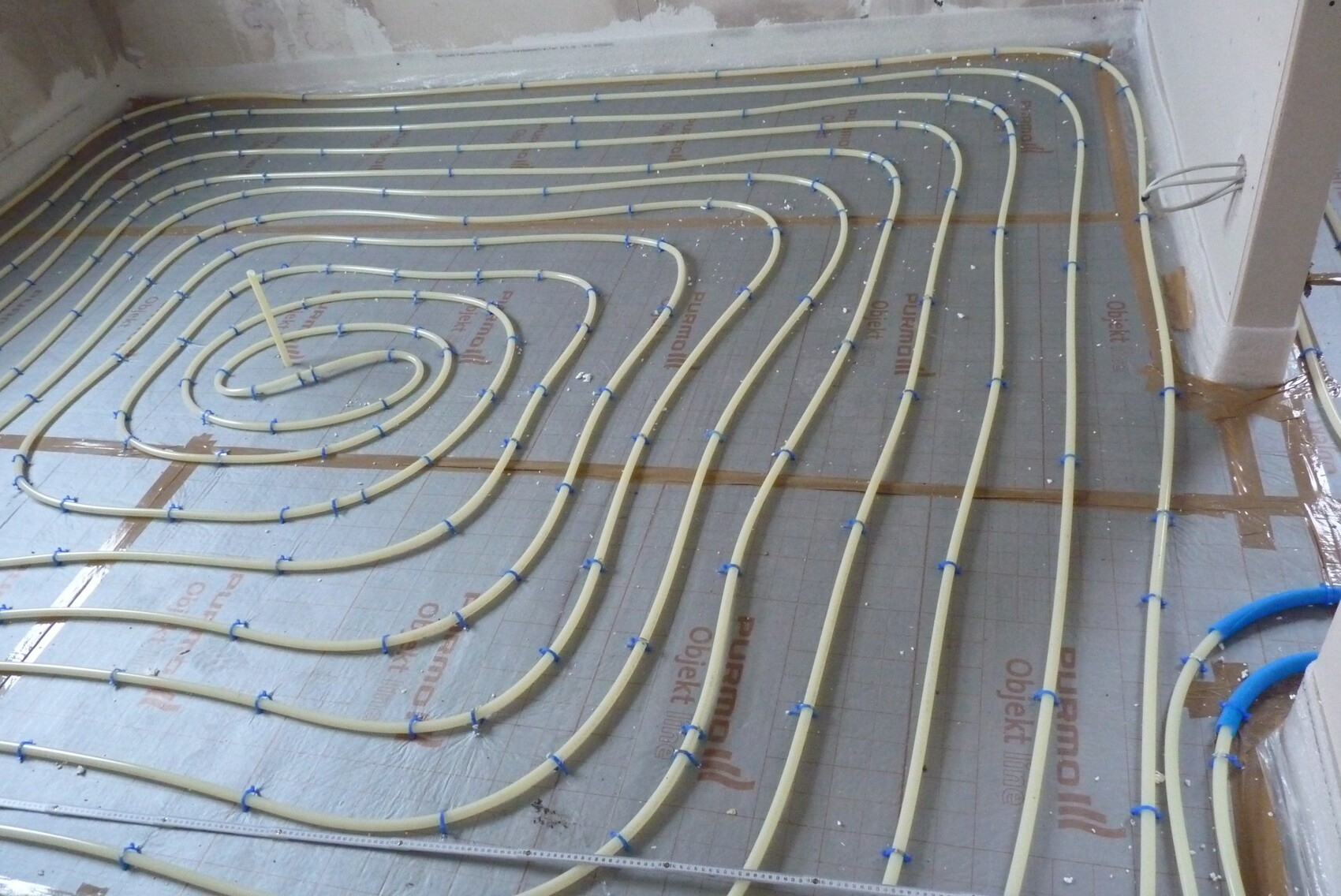 Unterflur-Heizungsrohre in spiralförmigen Schleifen auf Dämmplatte, blau geklipst verlegt.