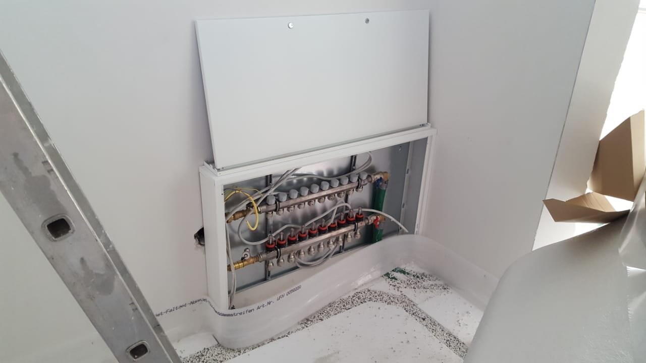 Offener Installationsschrank mit Rohrleitungen, Ventilen und Schläuchen einer Heizungsanlage.