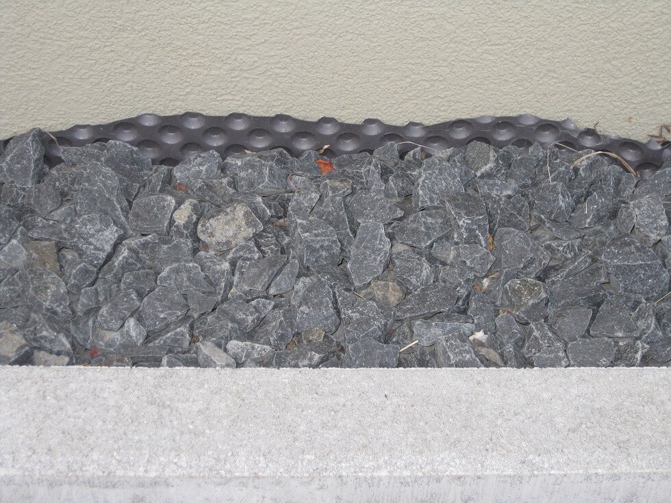 Gabionenwand aus Steinen am Fundament mit Betonboden und beige Gebäudewand
