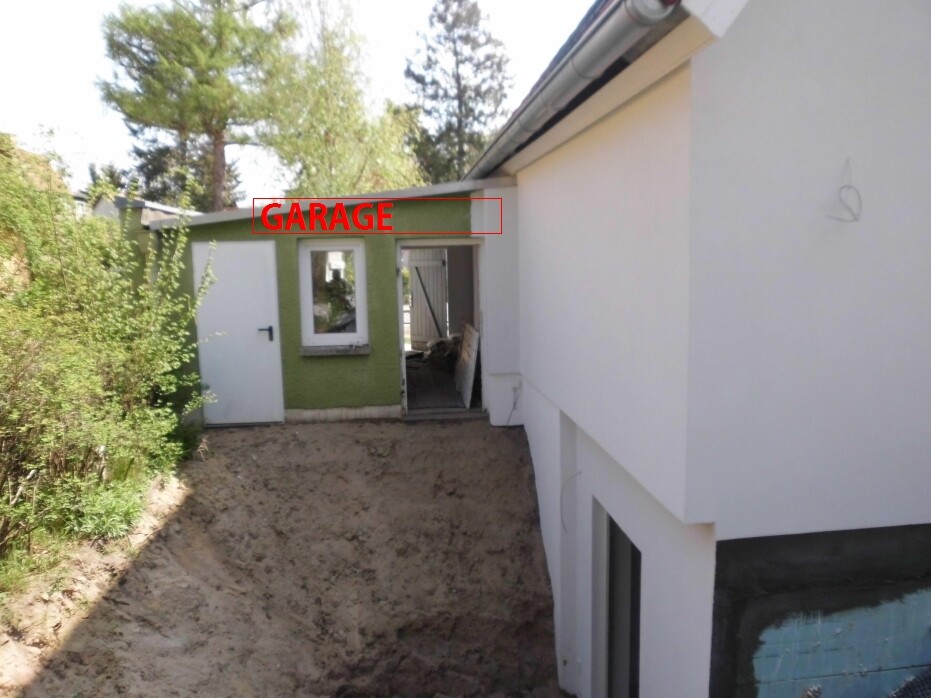 Außenansicht eines Hauses mit weißer Fassade, grüne Wand (Garage), offenes Tor davor