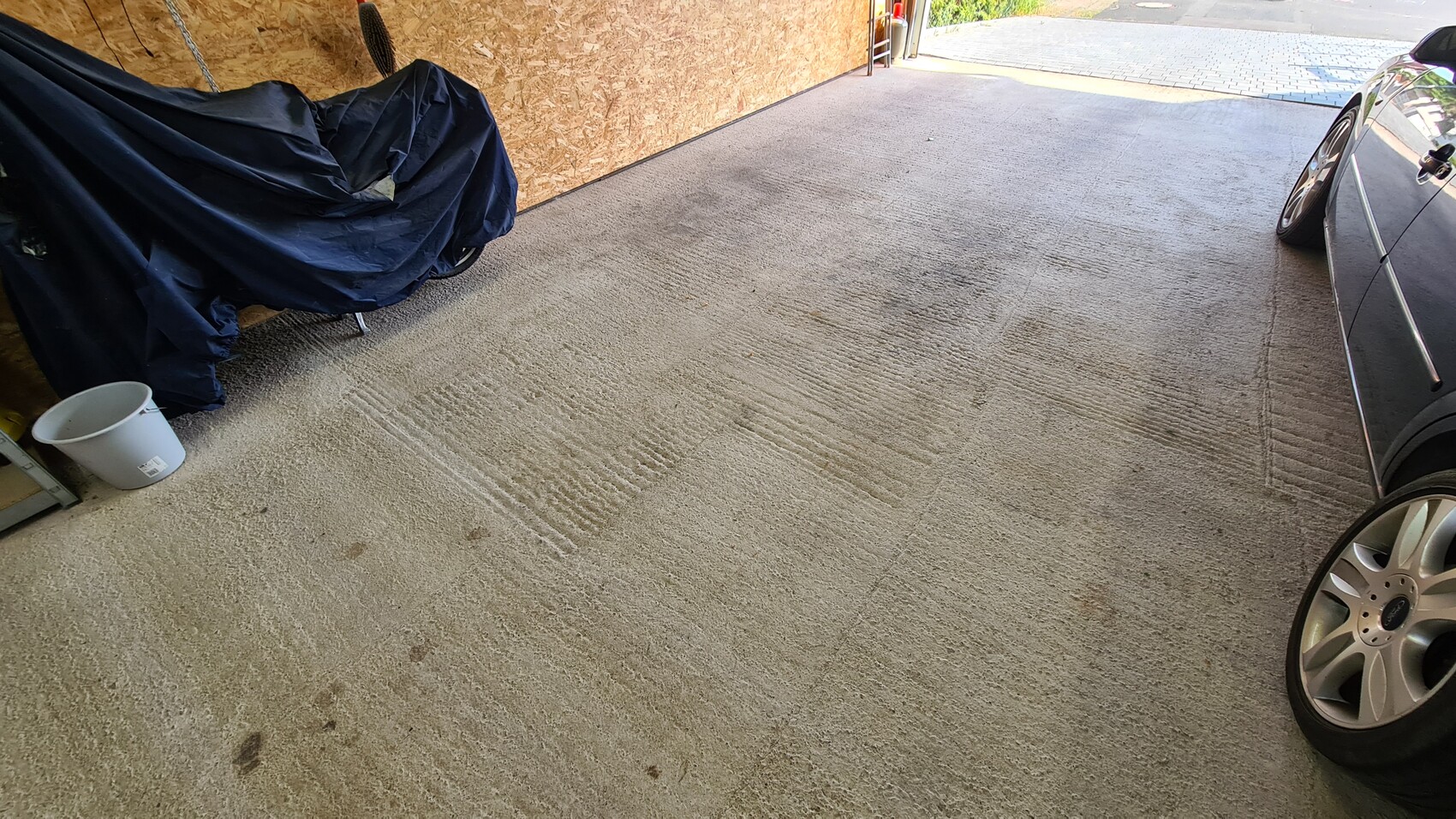 Garage mit blau abgedecktem Motorrad links neben einem geparkten Auto