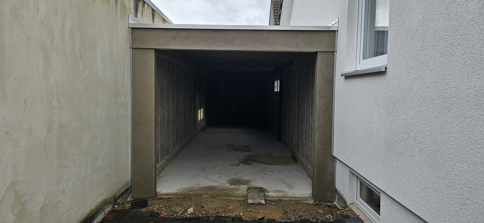 Dunkle Durchfahrt zwischen linker beigefarbenen Wand und rechter weißer Wand, führt ins Dunkel.