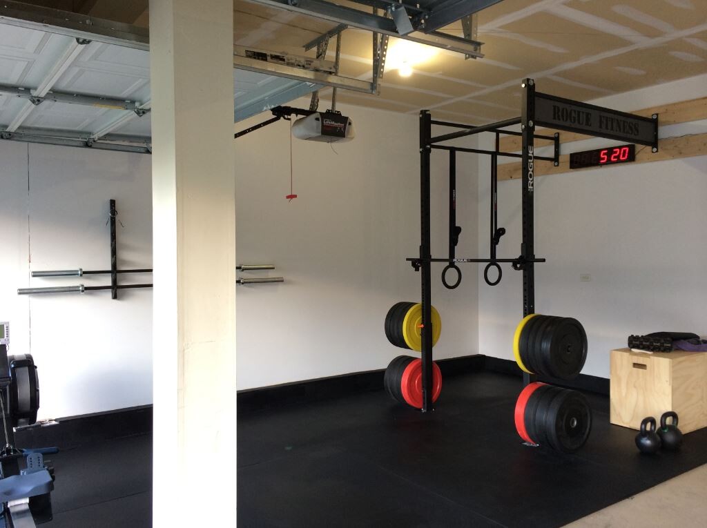 Kraftstation mit Squat-Rack, Hantelscheiben in Rot/Gelb, Ringe, Zeitanzeige 5:20, Rogue Fitness.