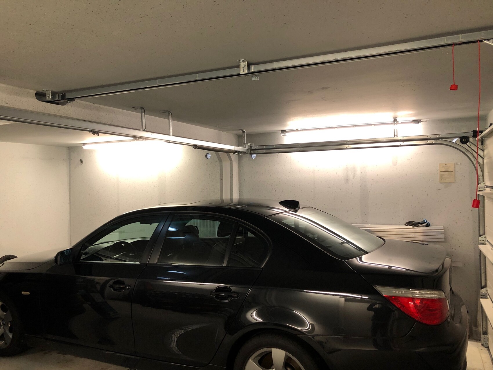 Schwarzes Auto in einer hellen Garage mit Decken-Rail-System und roter Zugleine.