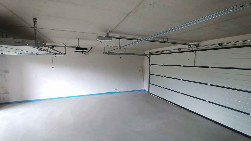 Leere Garage im Rohbau mit Betonboden, unbehandelter Decke und Torbereich