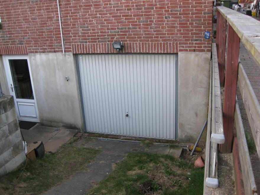 Garage mit grauem Rolltor, Seiteneingangstür und roter Backsteinfassade