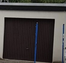 Braunes Garagen-Tor vor cremefarbener Wand, blaue Stützen im Vordergrund.